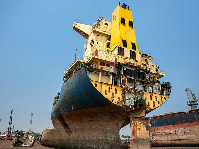 Crane lifting parts from the stern of a decommissioned vessel for scrap metal in a green ship recycle shipyard