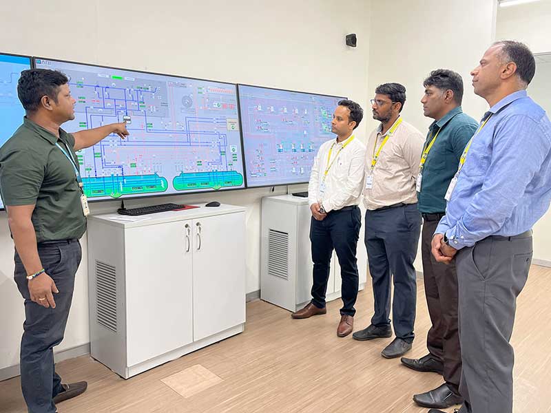 Instructor guiding four trainees through a methanol fuel system simulation on large digital screens during a classroom session