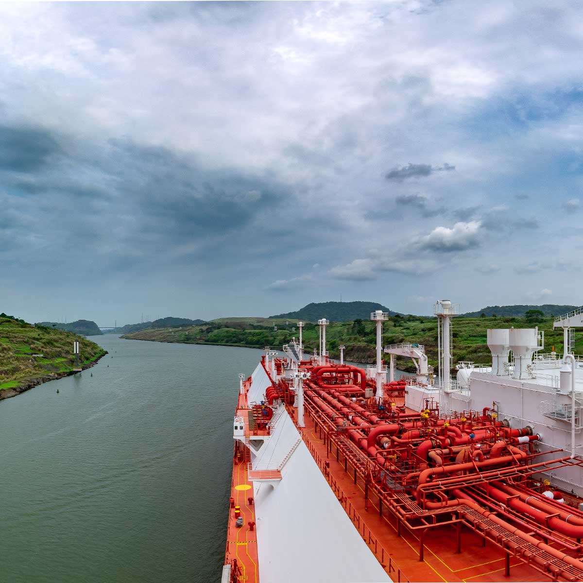 Red and white liquefied natural gas tanker navigating a narrow canal under a cloudy sky