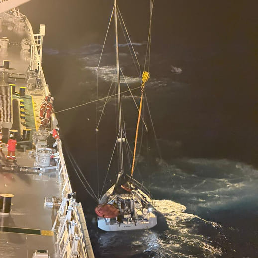 Nighttime rescue scene showing the distressed sailing vessel being lifted alongside KUFRA in rough seas