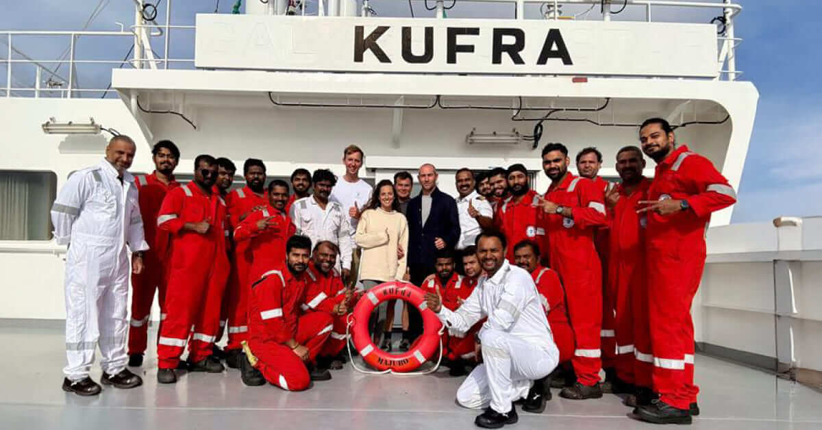 Crew of MT KUFRA standing with the four rescued individuals on bridge wings, smiling together for a group photo.